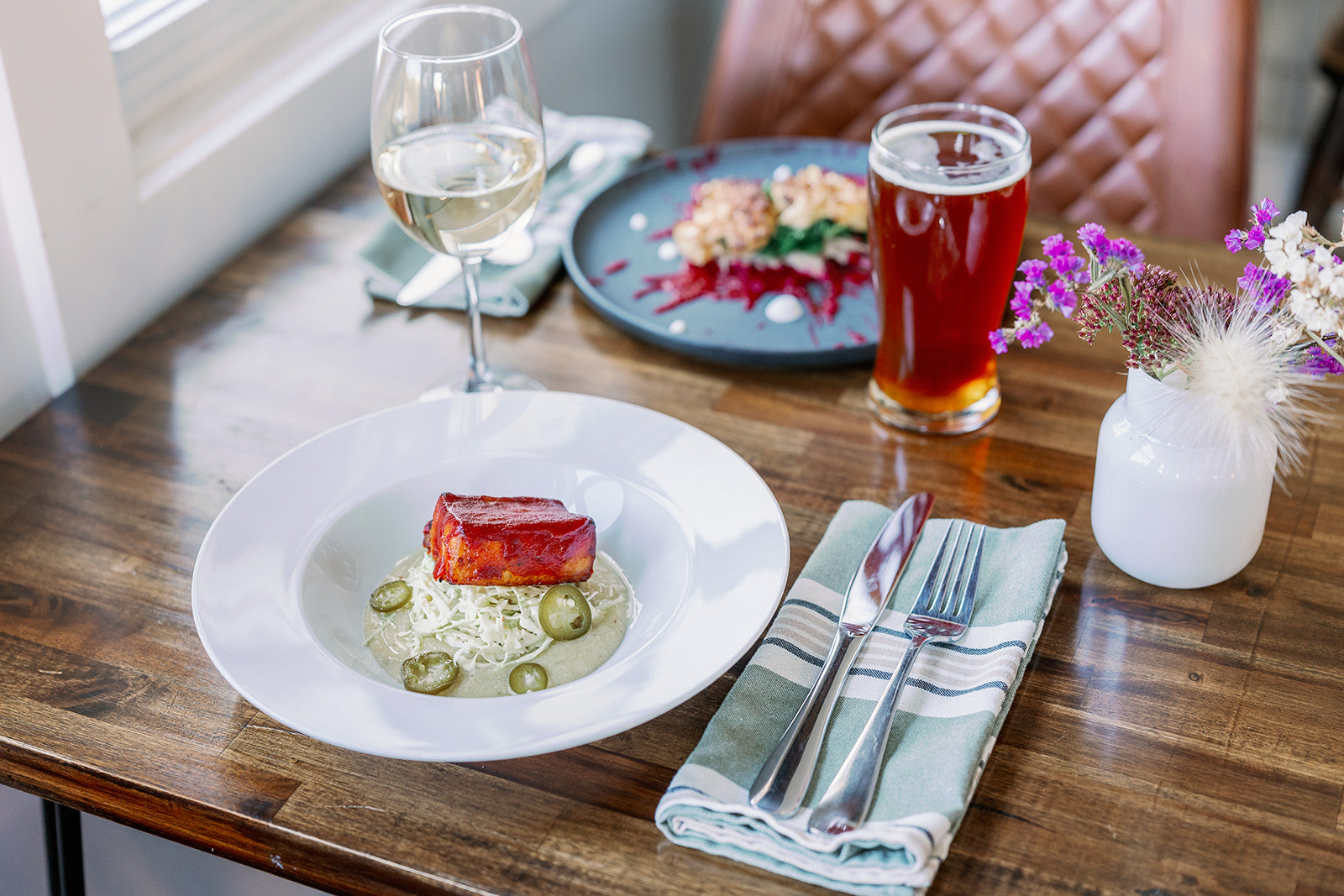 Dinner table setting with a dish, wine glass, and beer on a wooden table.