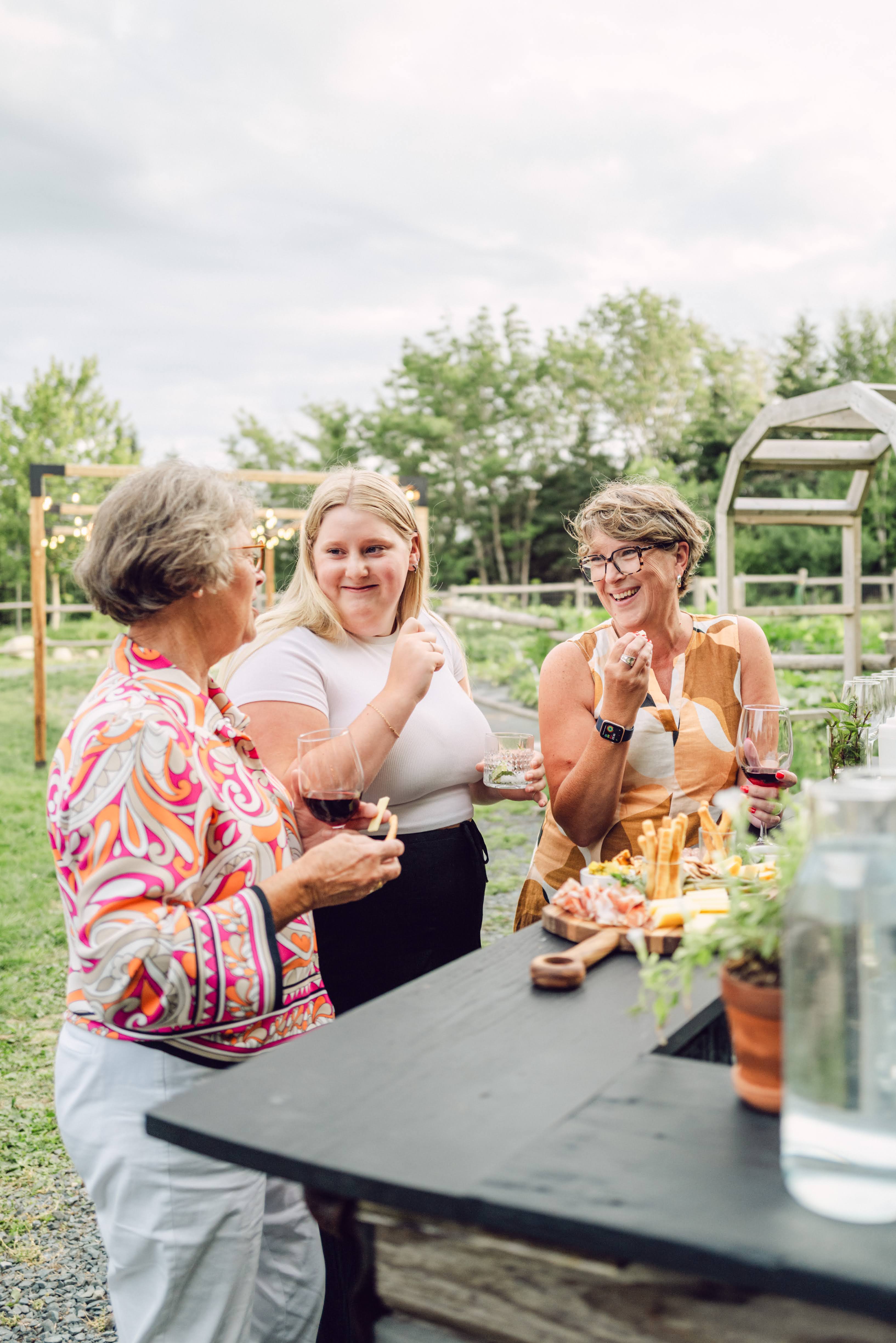 Three women sitting around a table outdoors, enjoying drinks and food.