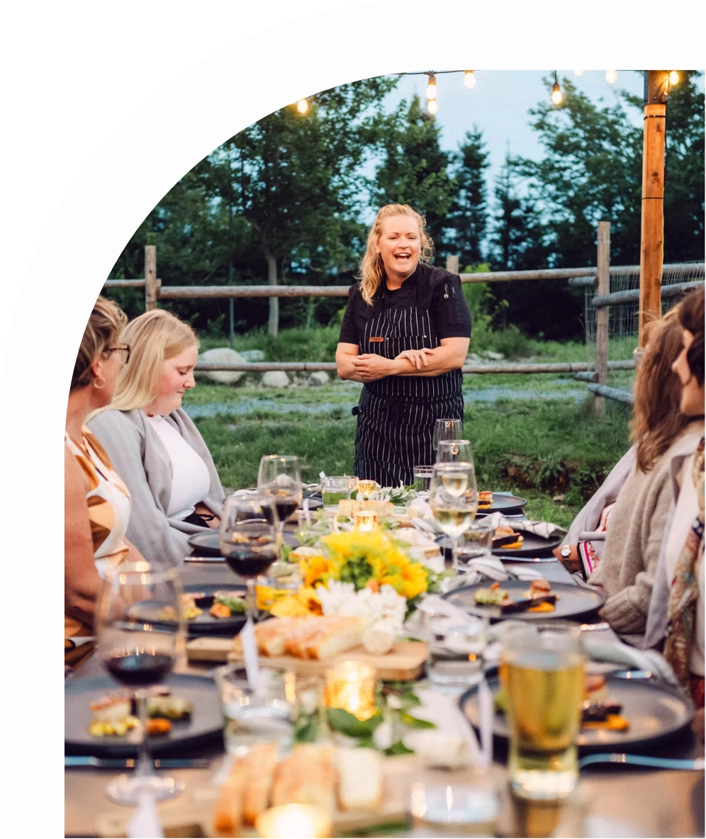 Chef Kim standing at a dinner table outdoors with guests, surrounded by nature.