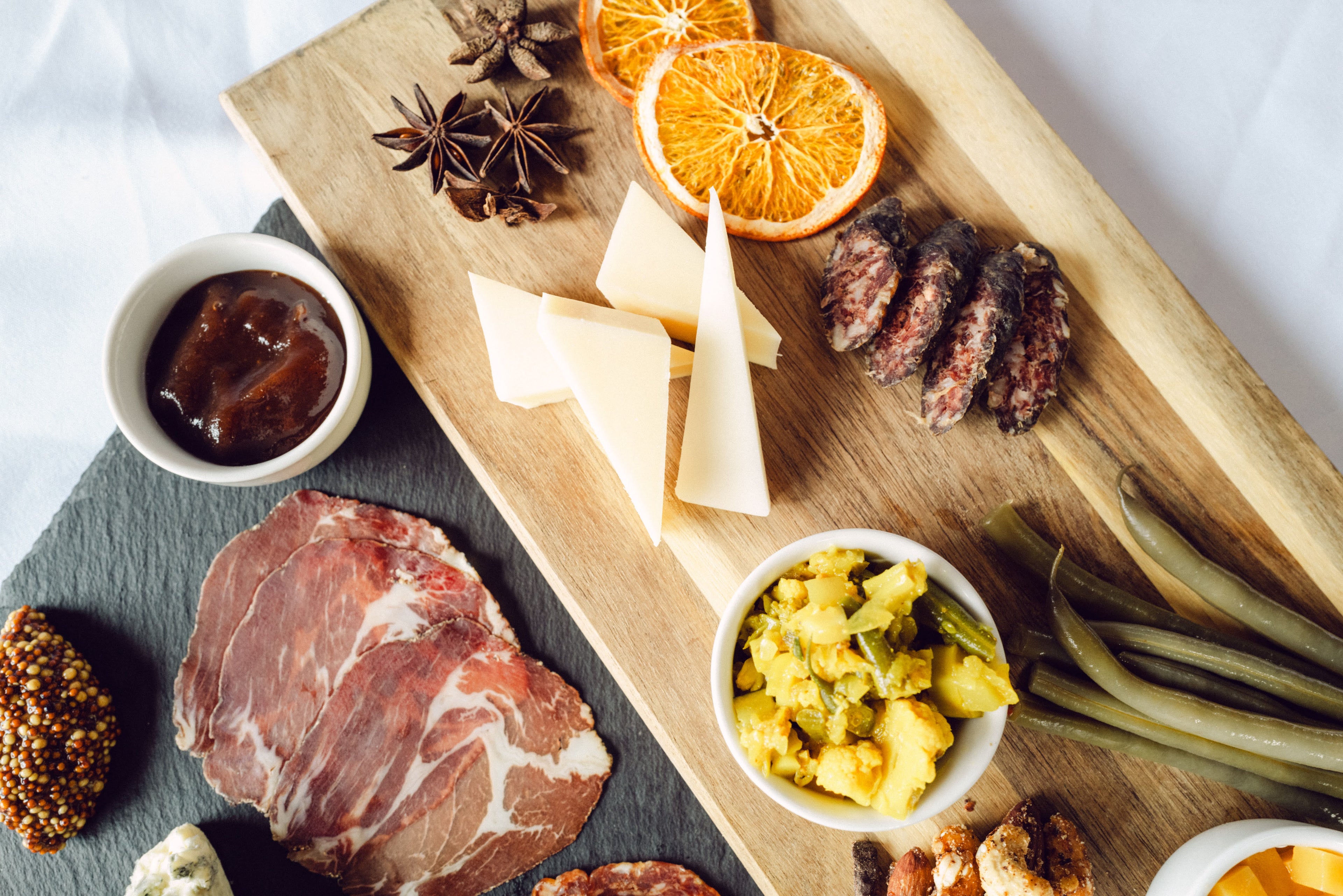 Wooden cutting board with assorted meats, cheeses, and pickles on a white background