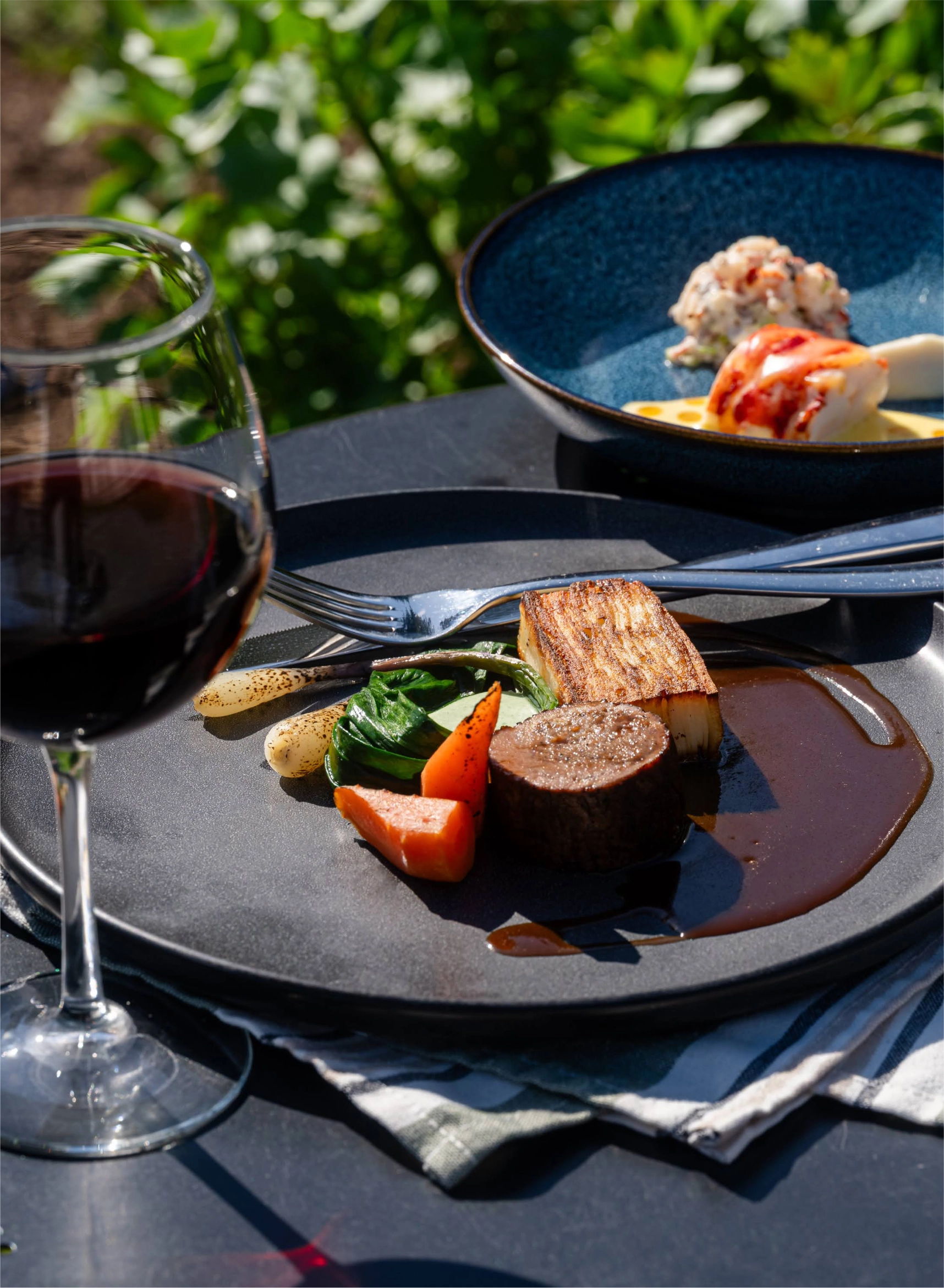 Dinner setting with a plate of food, a glass of red wine, and a garden in the background.