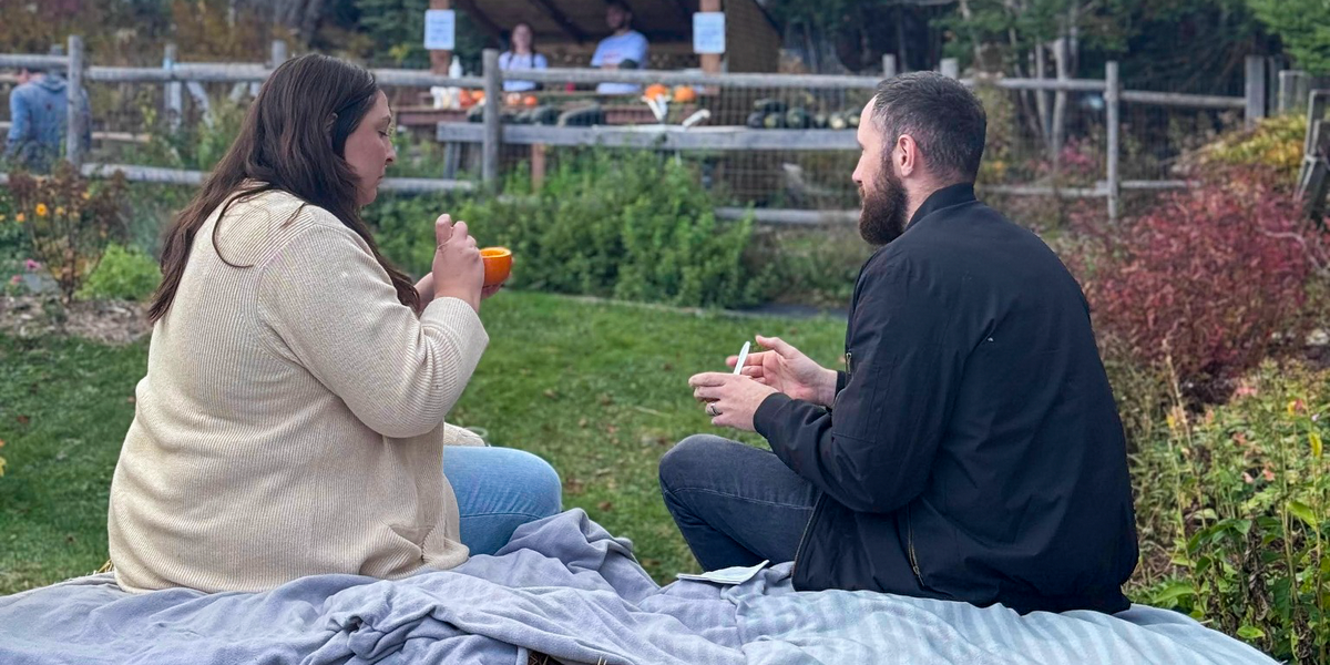 Two guests enjoying food while seated on a blanket-covered hay bale in Lupin’s garden.