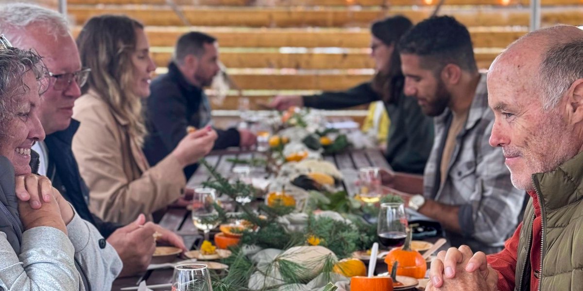 Guests sharing food and conversation at a long outdoor table decorated with pumpkins and greenery.