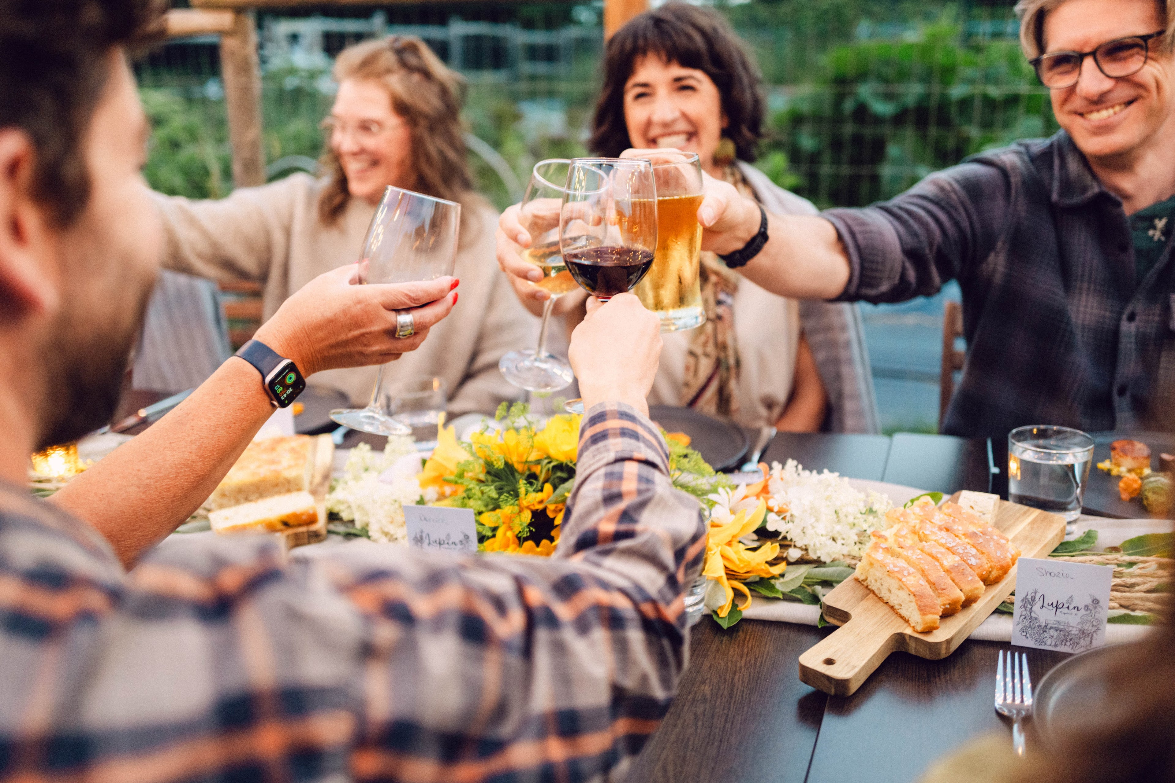 Group of people toasting with drinks at a outdoor dinner table.