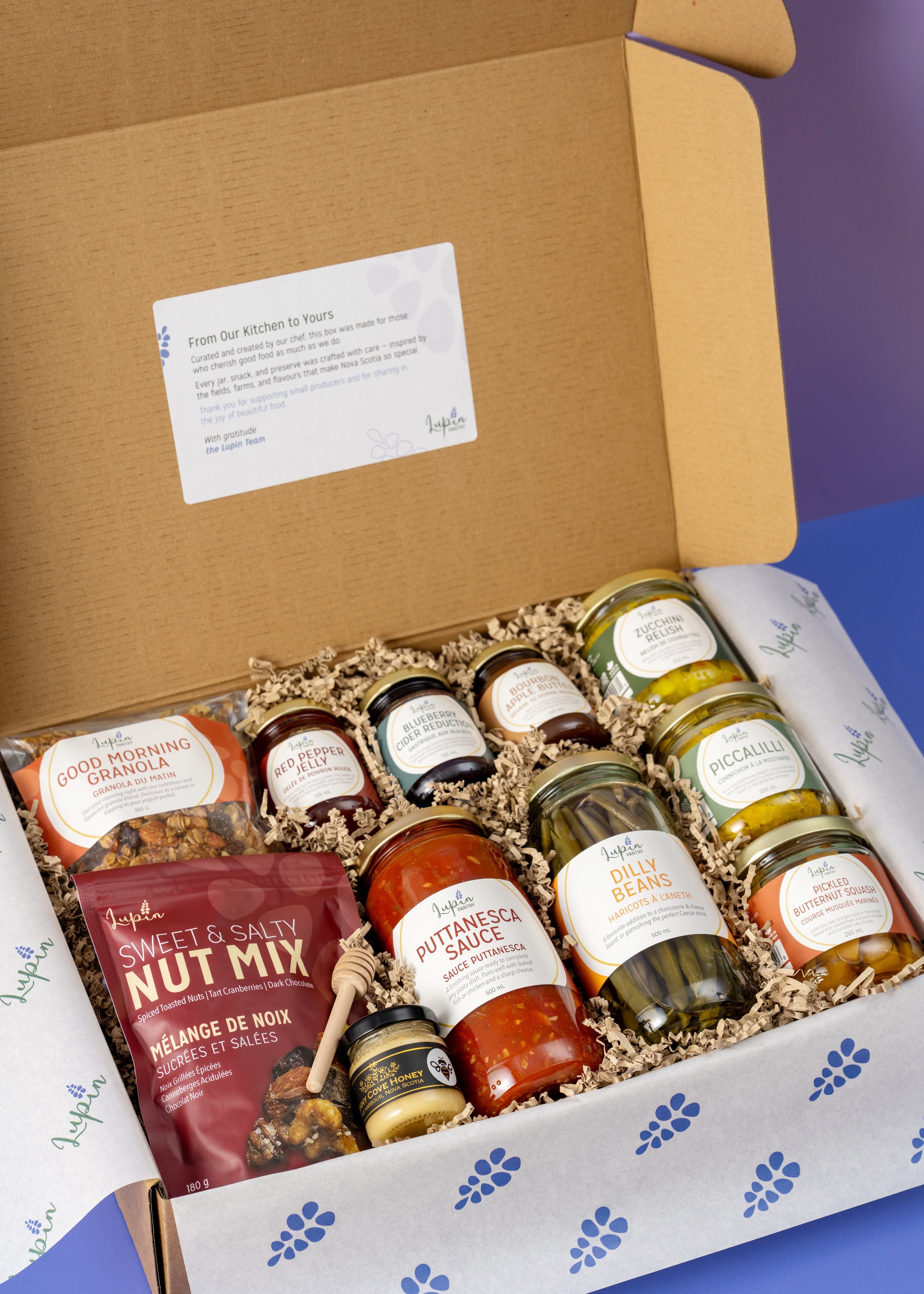 Open box containing various food items including jars and a bag on a blue background