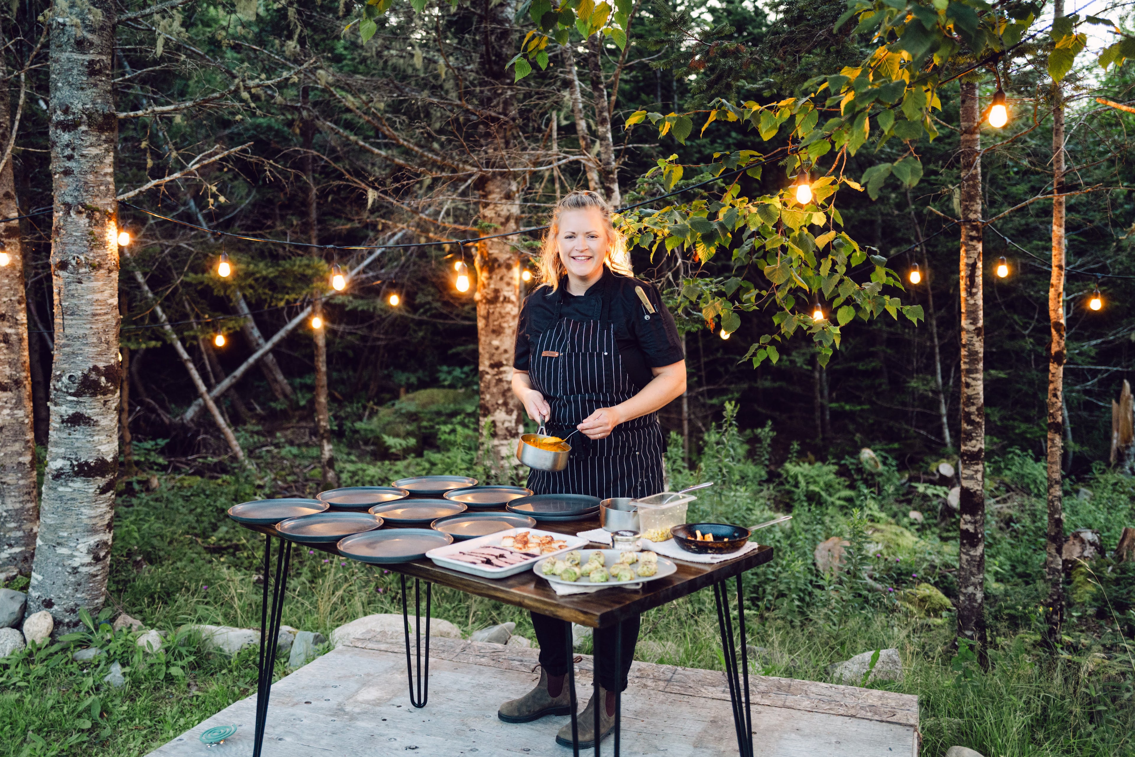 Chef Kim standing by a table with food in an outdoor garden setting in early evening.