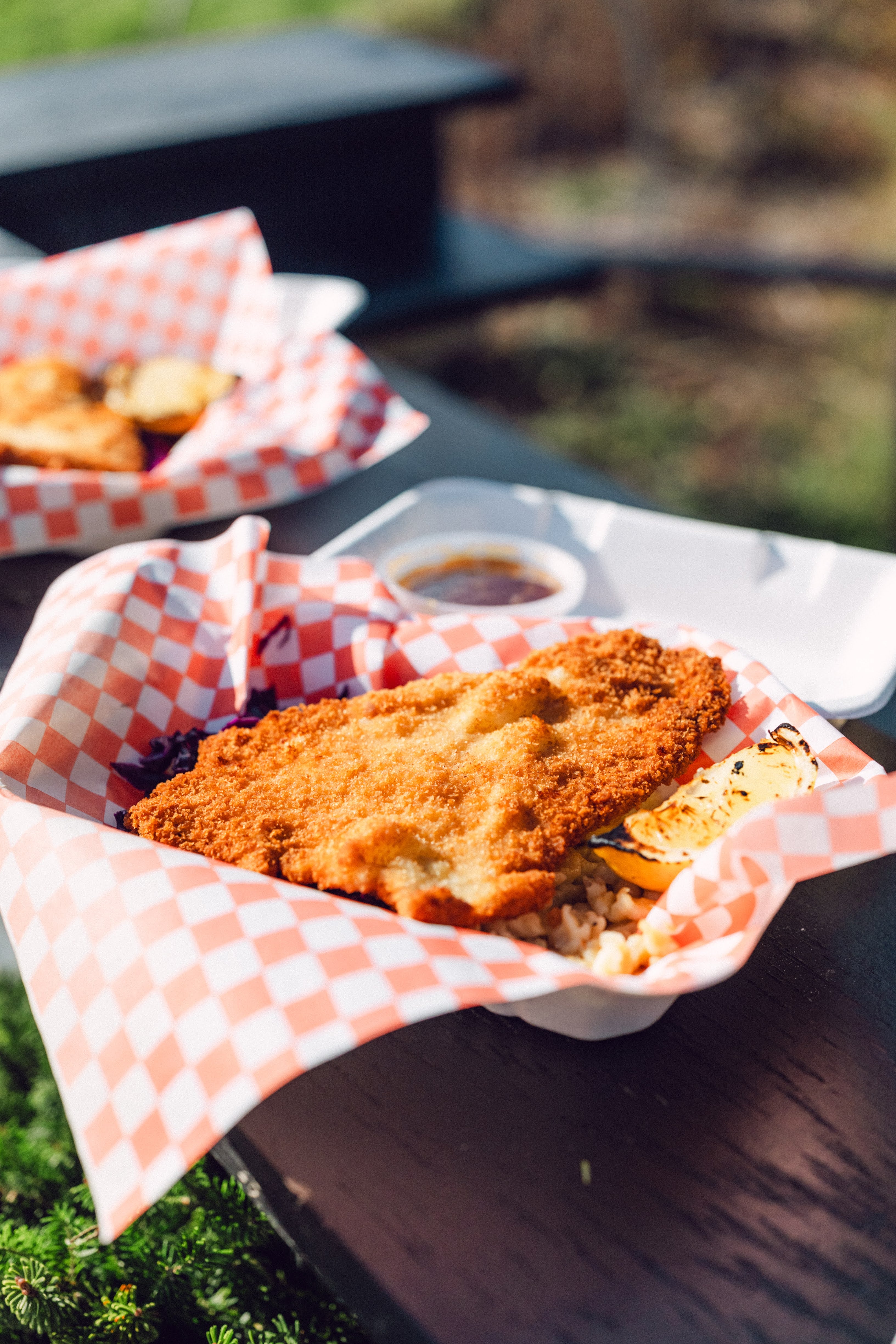 Fried fish dish on checkered paper with a side of sauce on a table outdoors.